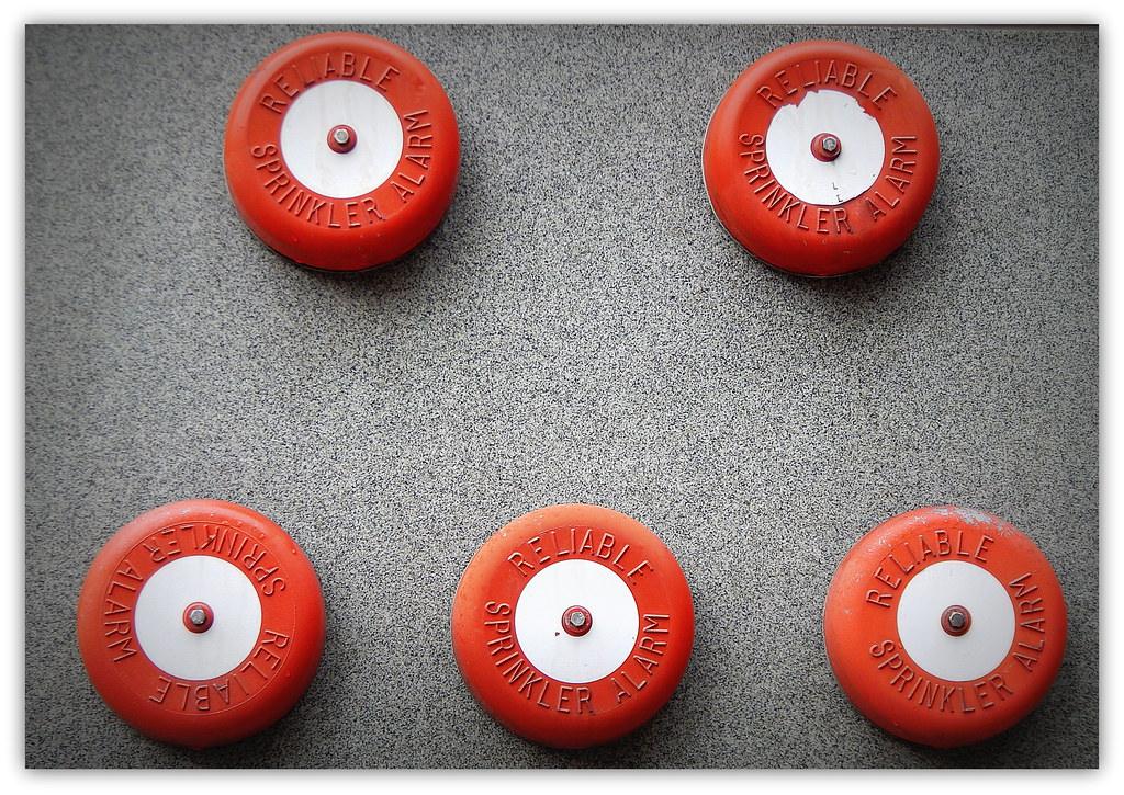 Five red sprinkler alarm bells on a grey wall